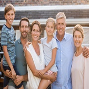 Portrait of cheerful extended family standing outside their house. Happy family standing outside and looking at camera. Parents with grandparents e children enjoying vacation together.